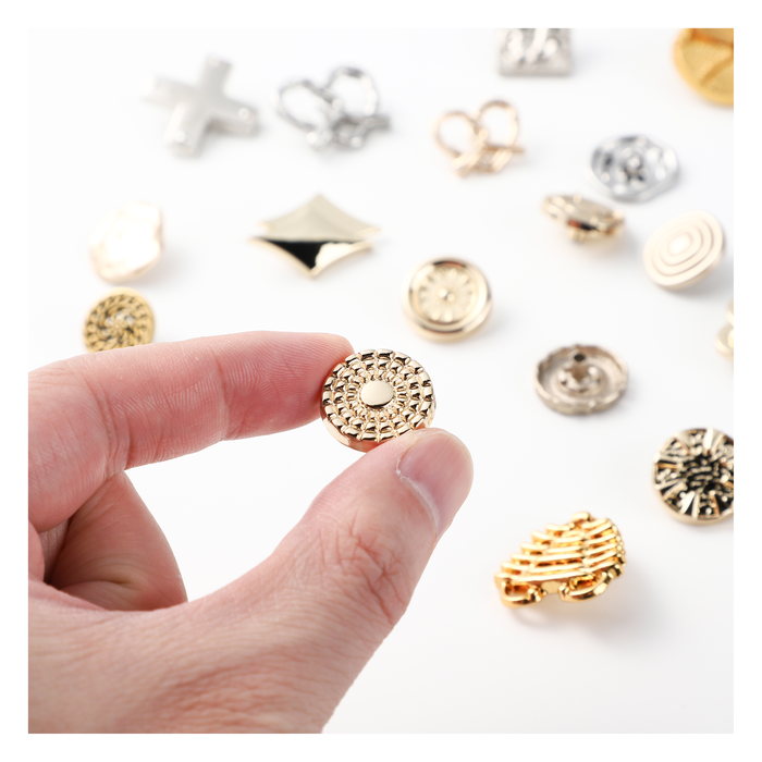 Hand holding a gold shank button among assorted metal buttons